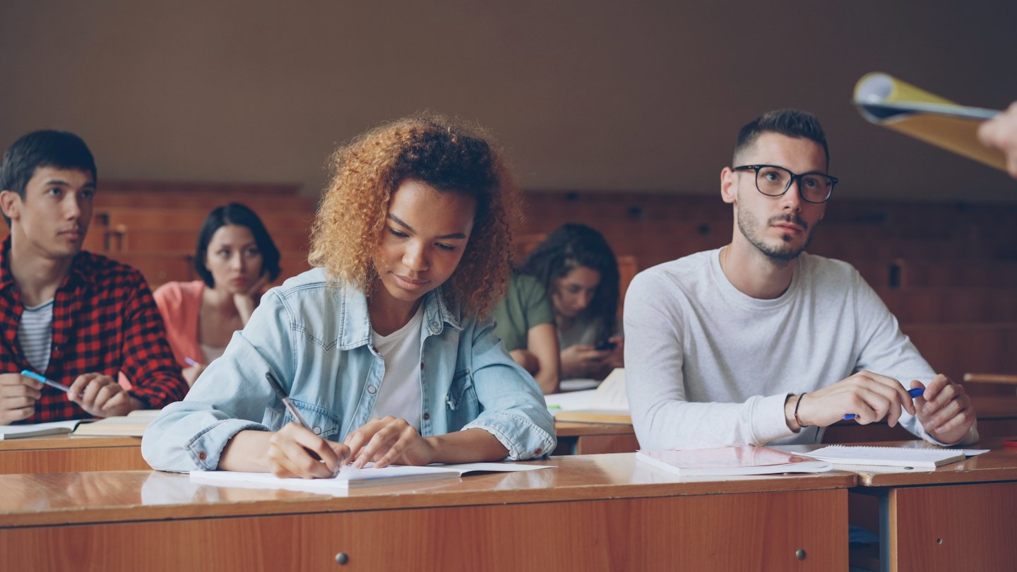University students listen to a lecture in a wooden lecture hall.